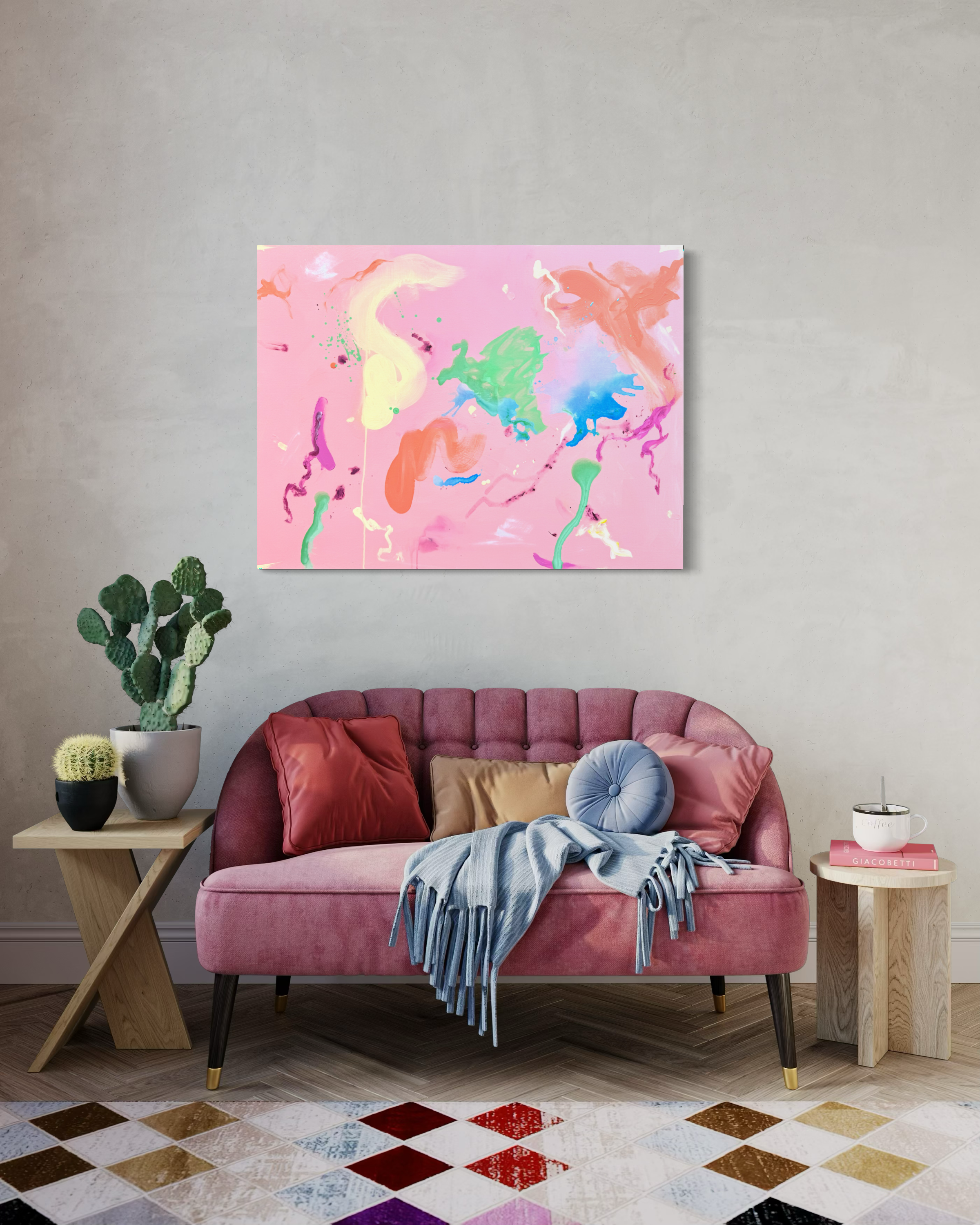 A pink sofa with pillows, with a blanket draped over it, flanked by two wooden side tables with plants and a coffee mug, in front of a concrete wall with colorful abstract artwork, and a multicolored tile floor.