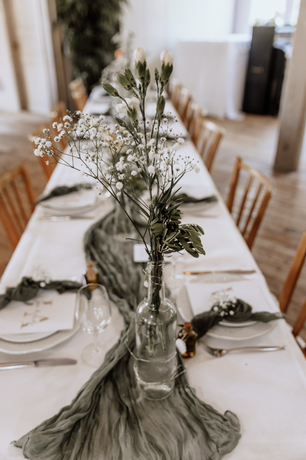 Blumenstrauß mit weißen und grünen Blumen in einer Glasvase auf einem festlich gedeckten Tafel Tisch.