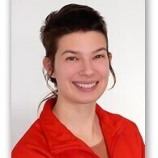 A young woman with short dark hair in a messy style, smiling, wearing a red jacket against a plain white background.