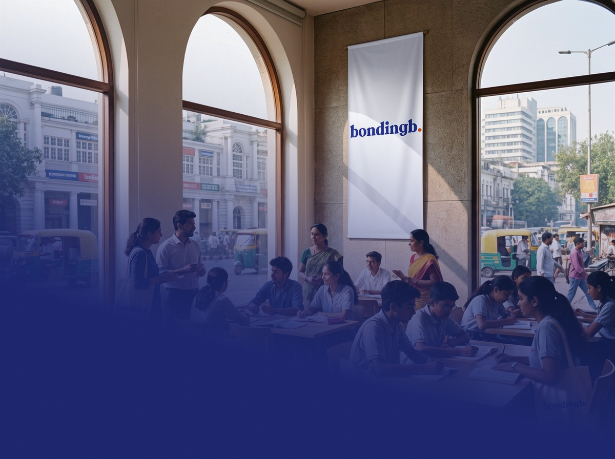 People gathered inside a spacious room with large arched windows, some standing and some sitting at tables, in a building with a city street view outside. There is a white banner on the wall with the word 'bondingb.' in blue.