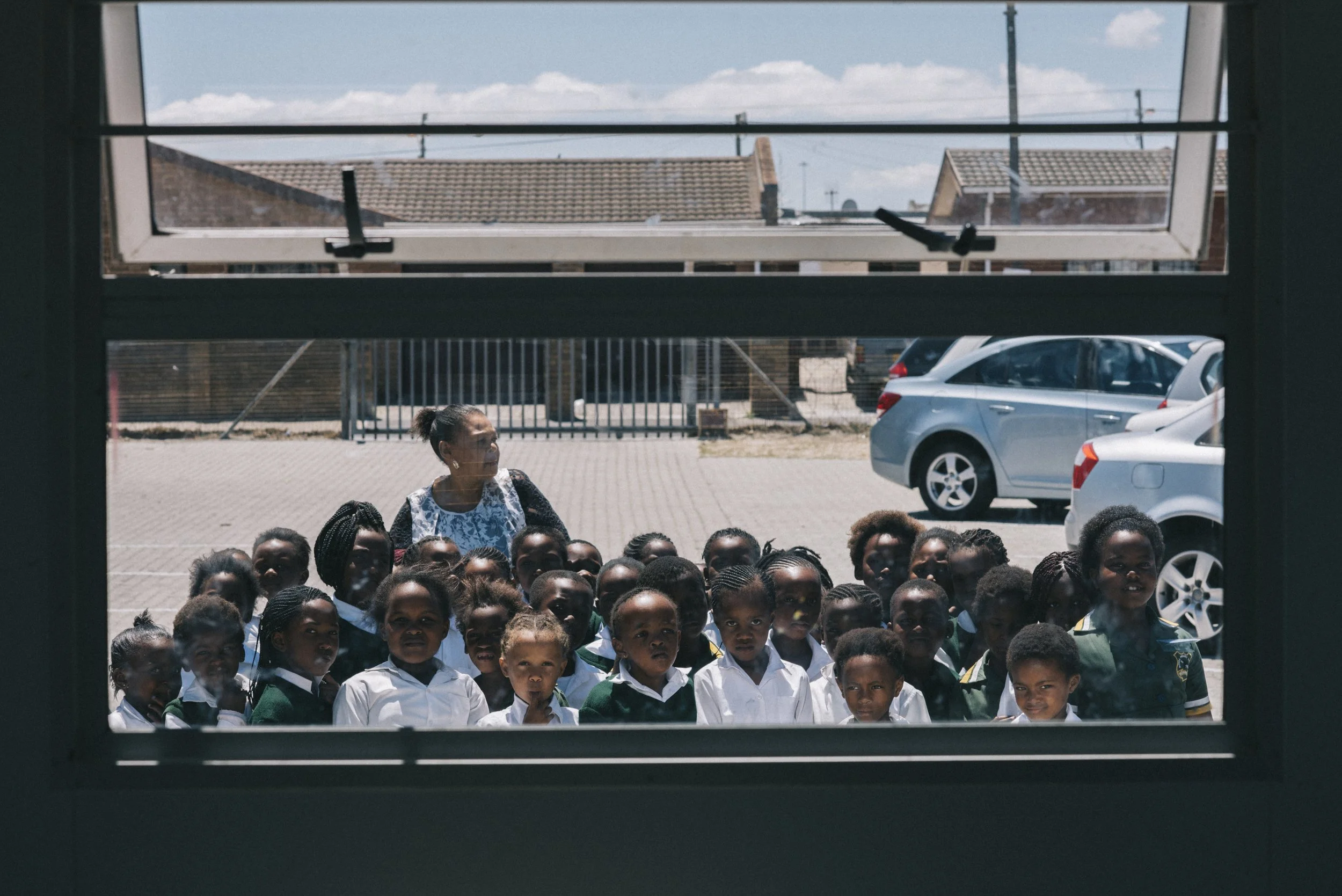 Gruppe von Kindern, die durch ein Fenster schauen, draußen auf einem Schulhof bei sonnigem Wetter