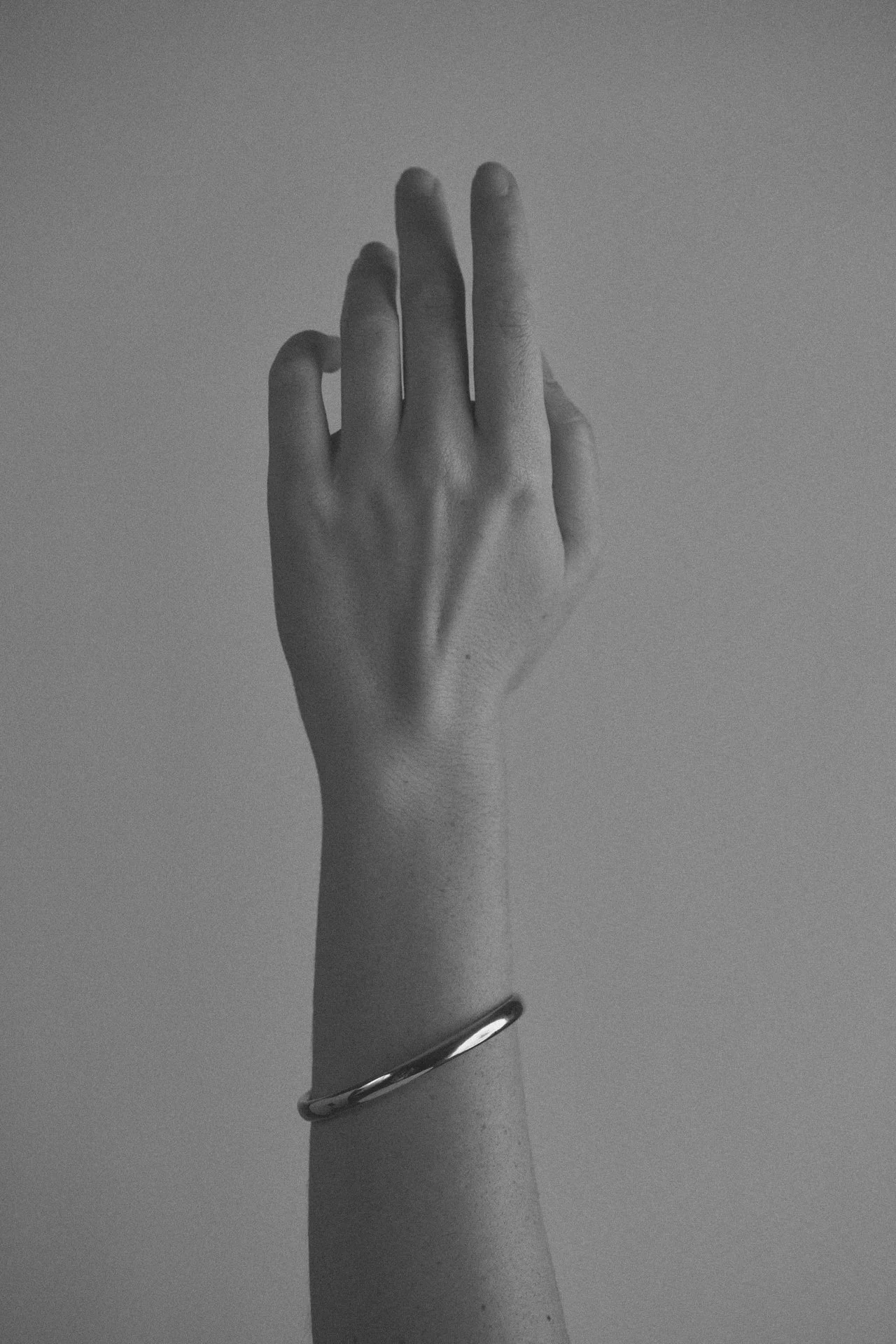 Schwarz-Weiß-Bild einer Hand mit einem Arm, der einen einfachen, runden Armreif trägt.