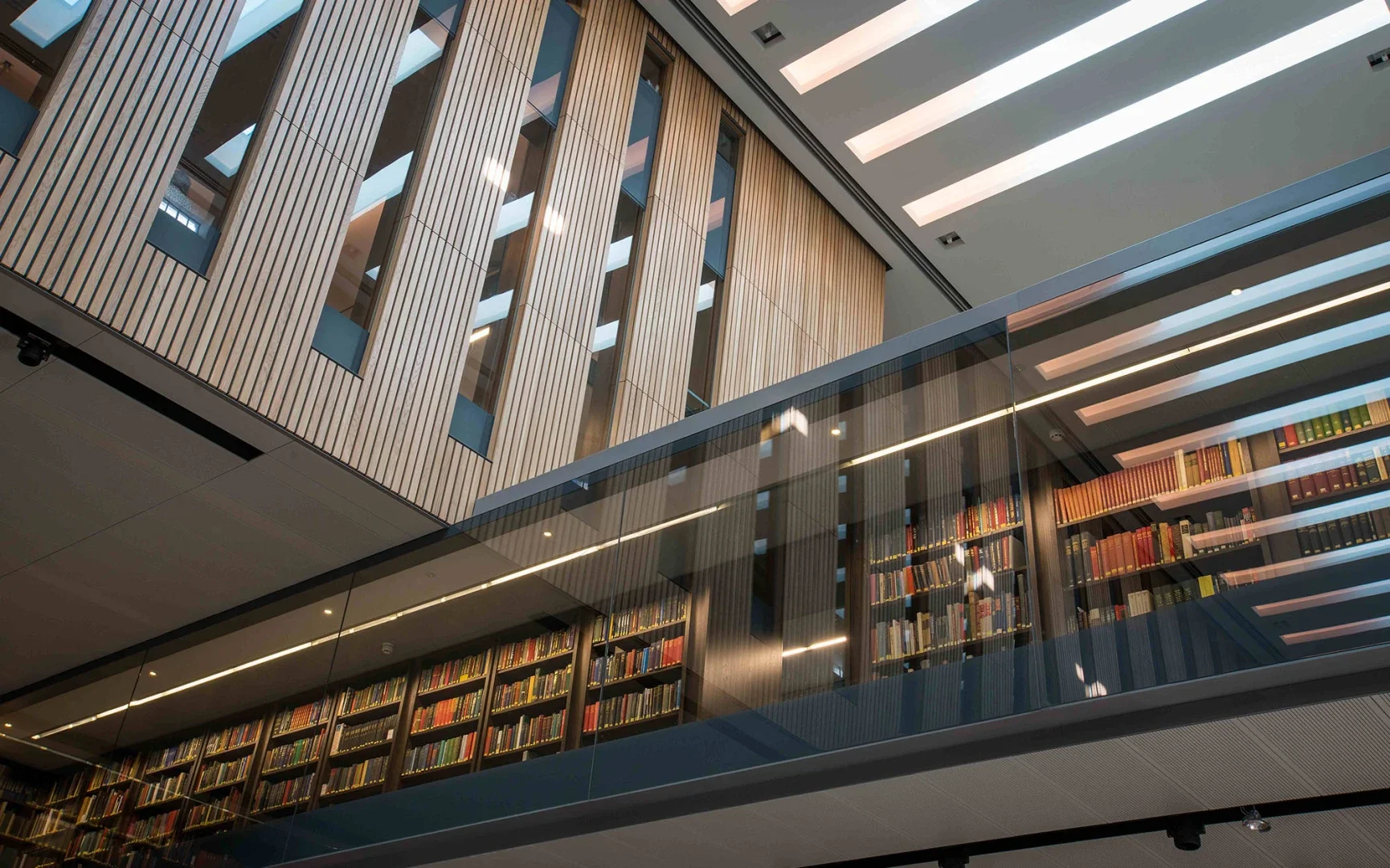 Interior view of a modern multi-story library with wooden panels, glass railings, and shelves filled with books.