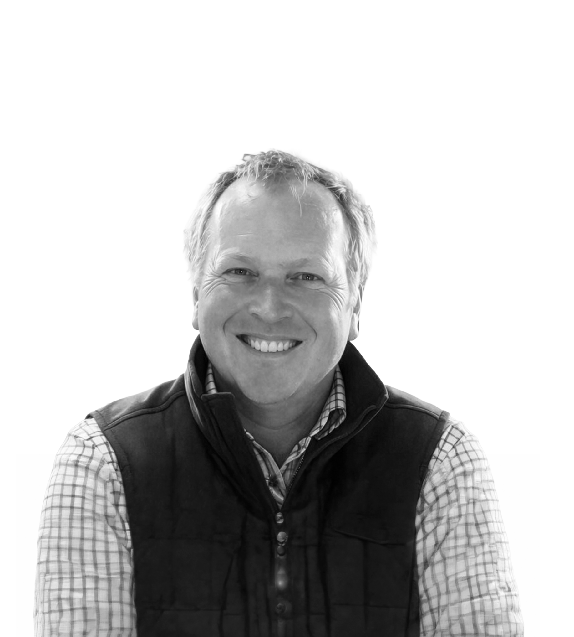 A smiling man wearing a checkered shirt and a dark vest, standing against a white background.