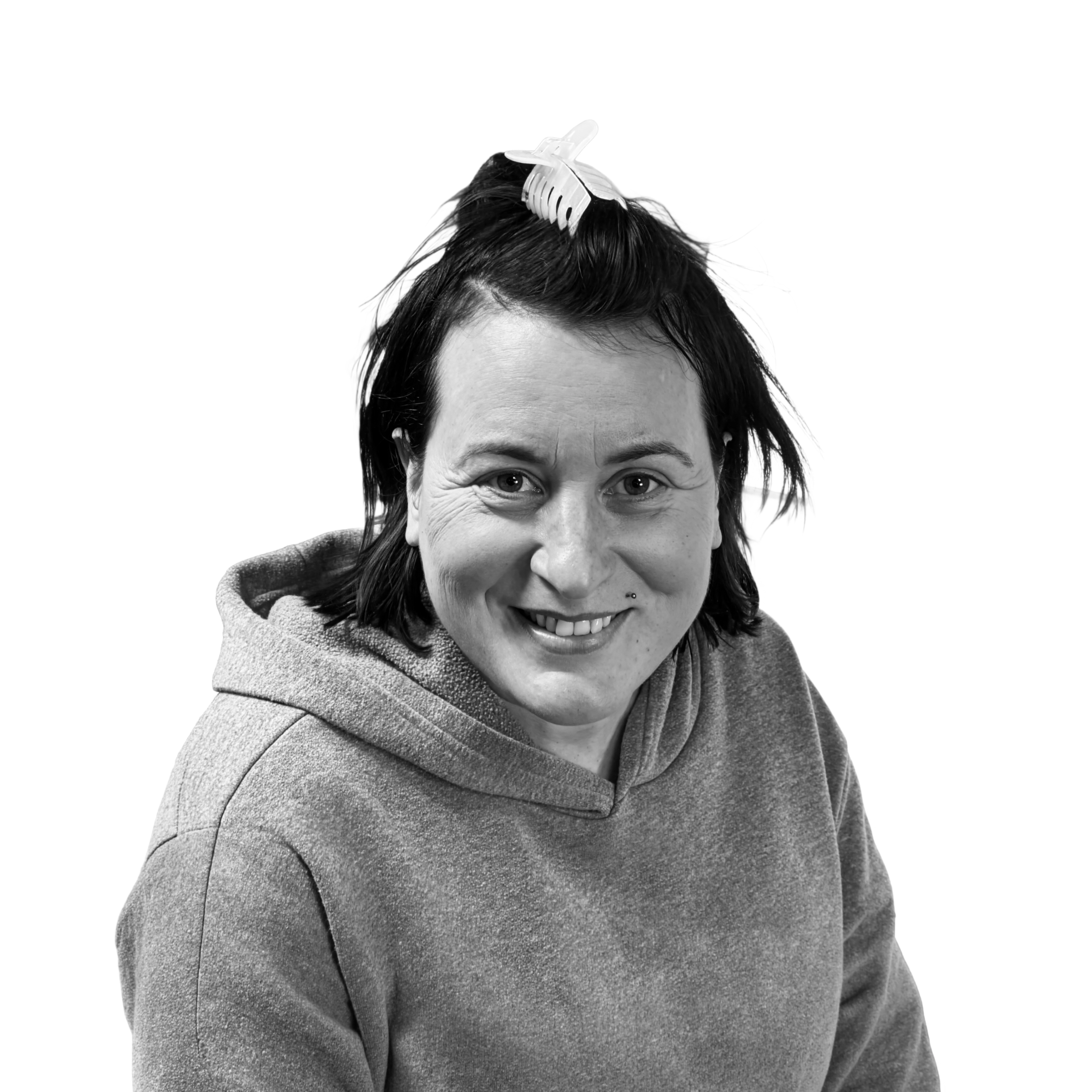 Black and white photo of a woman with dark hair, wearing a hoodie, smiling and looking at the camera, with a hair clip on top of her head.