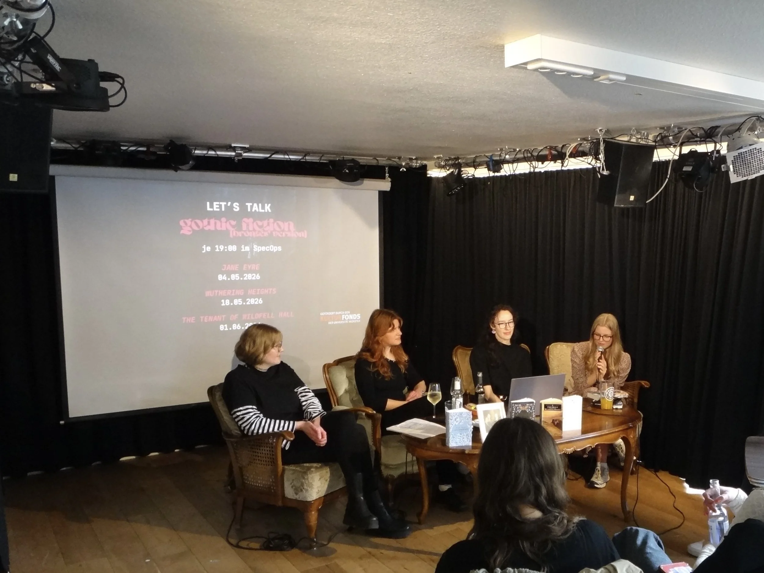 Die vier Zänkischen Littchen Friederike Krüger, Verena Meyer, Cilly Pola Krämer und Helena Wilde an einem Tisch mit einer Präsentation im Hintergrund