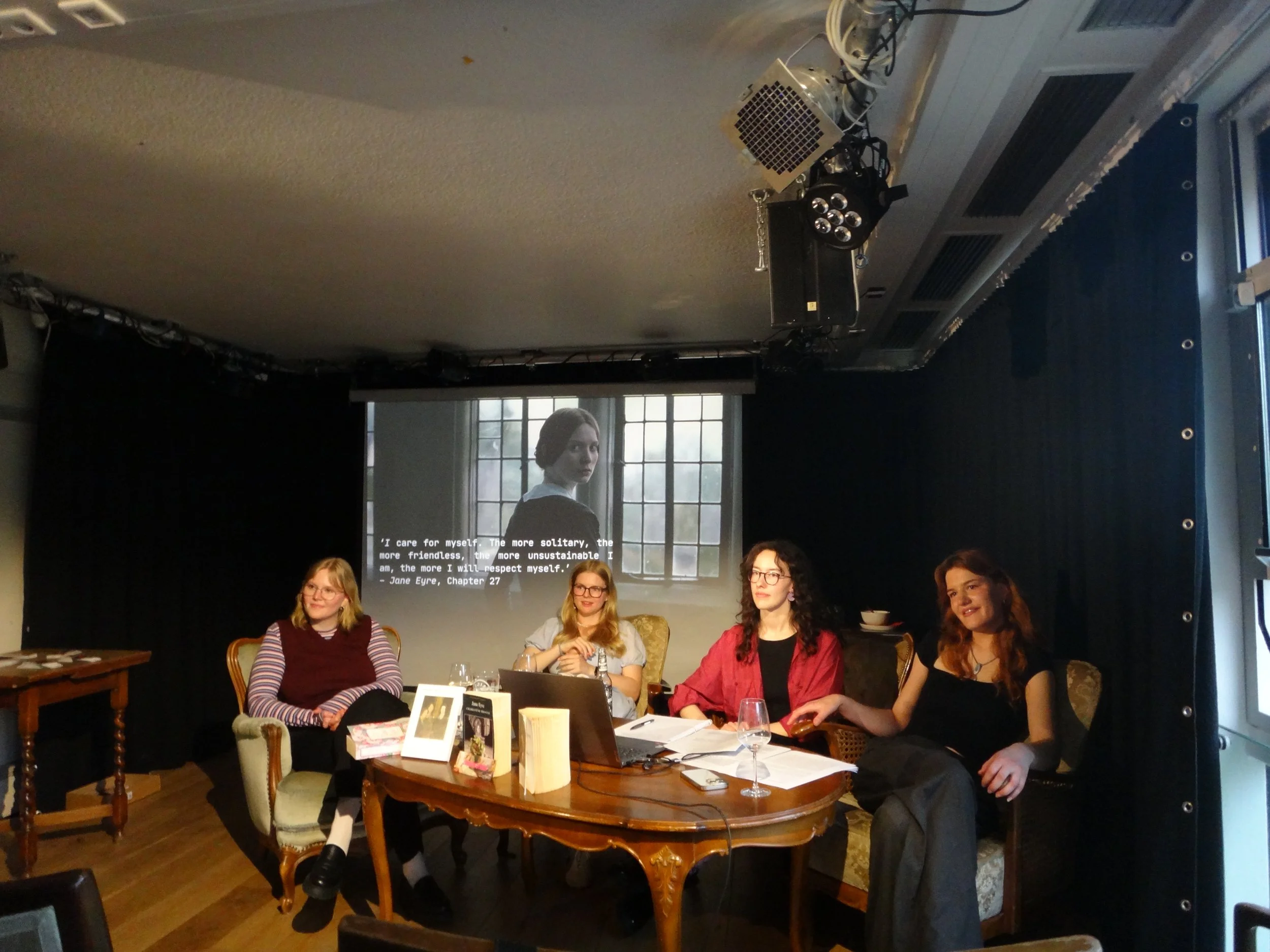 Die Zänkischen Littchen (Friederike Krüger, Helena Wilde, Cilly Pola Krämer und Verena Meyer) bei ihrer Veranstaltung 'GOTHIC FICTION (brontës' version) auf vier Stühlen mit einem Tisch voller Bücher, Gläser und einem Laptop