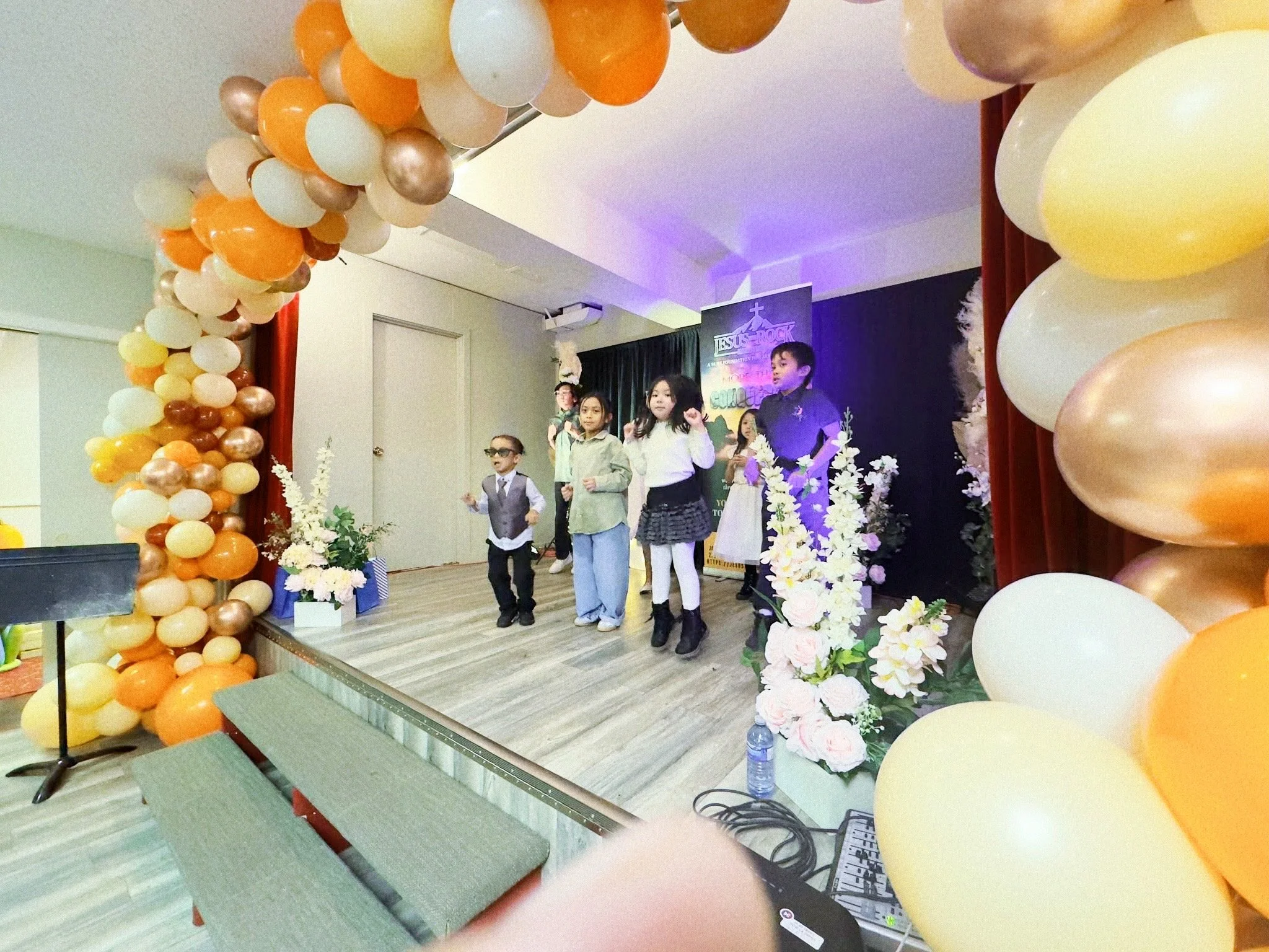 Children performing on stage decorated with balloons and floral arrangements at a children's church event