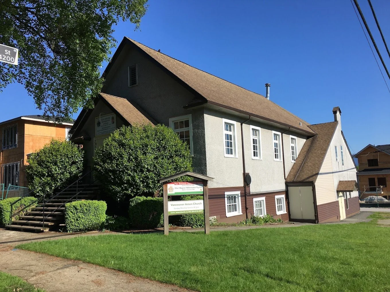 A church building with white and brown exterior, multiple windows, and a sign in front that reads Vancouver Church.