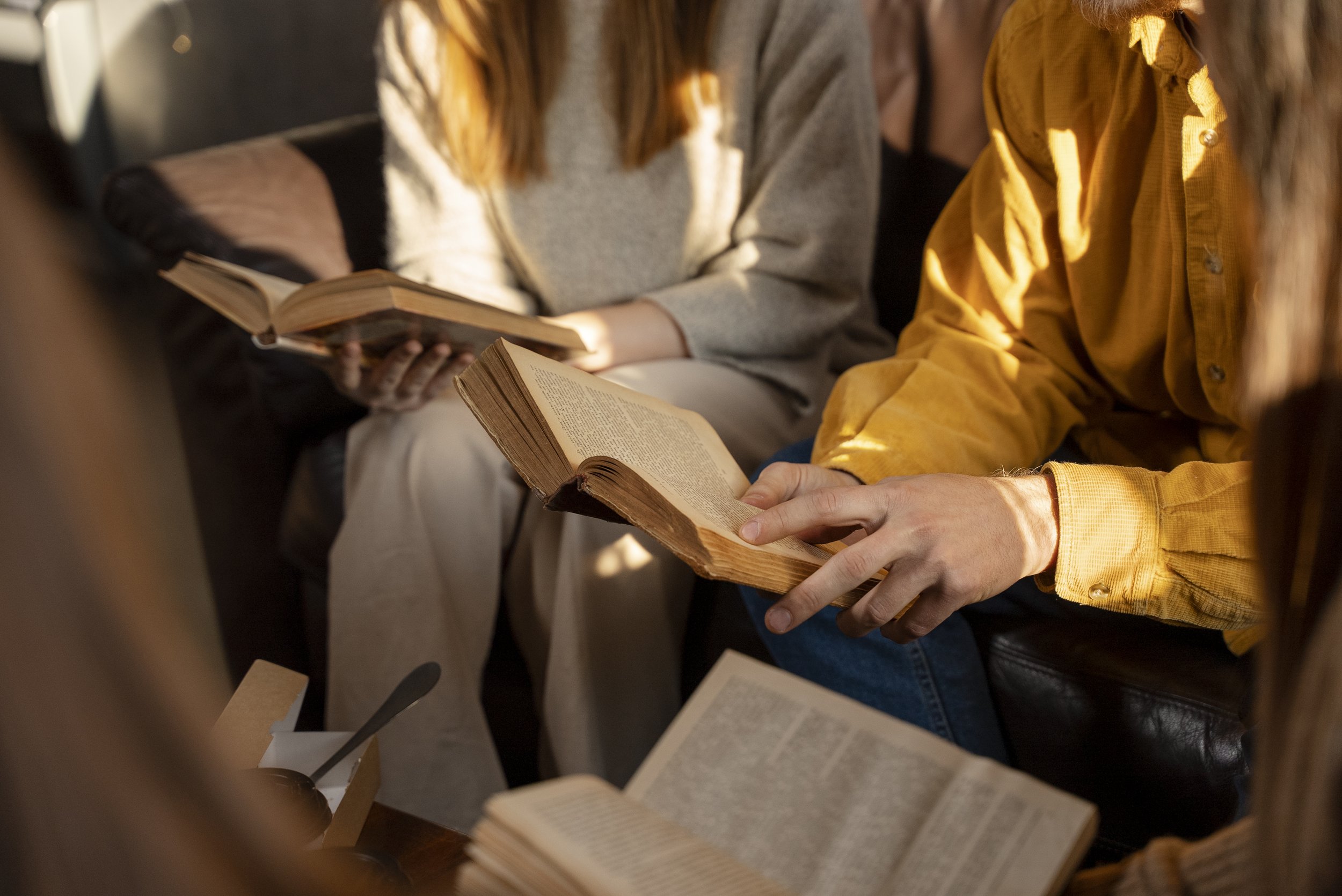 People sitting on a couch reading books, with warm lighting highlighting the books.