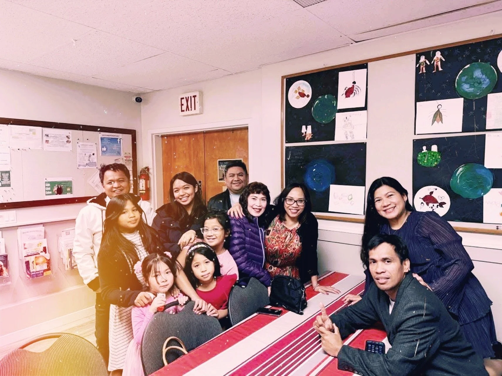 Group of adults and children gathered in a classroom with colorful artwork on the walls, smiling for a photo.