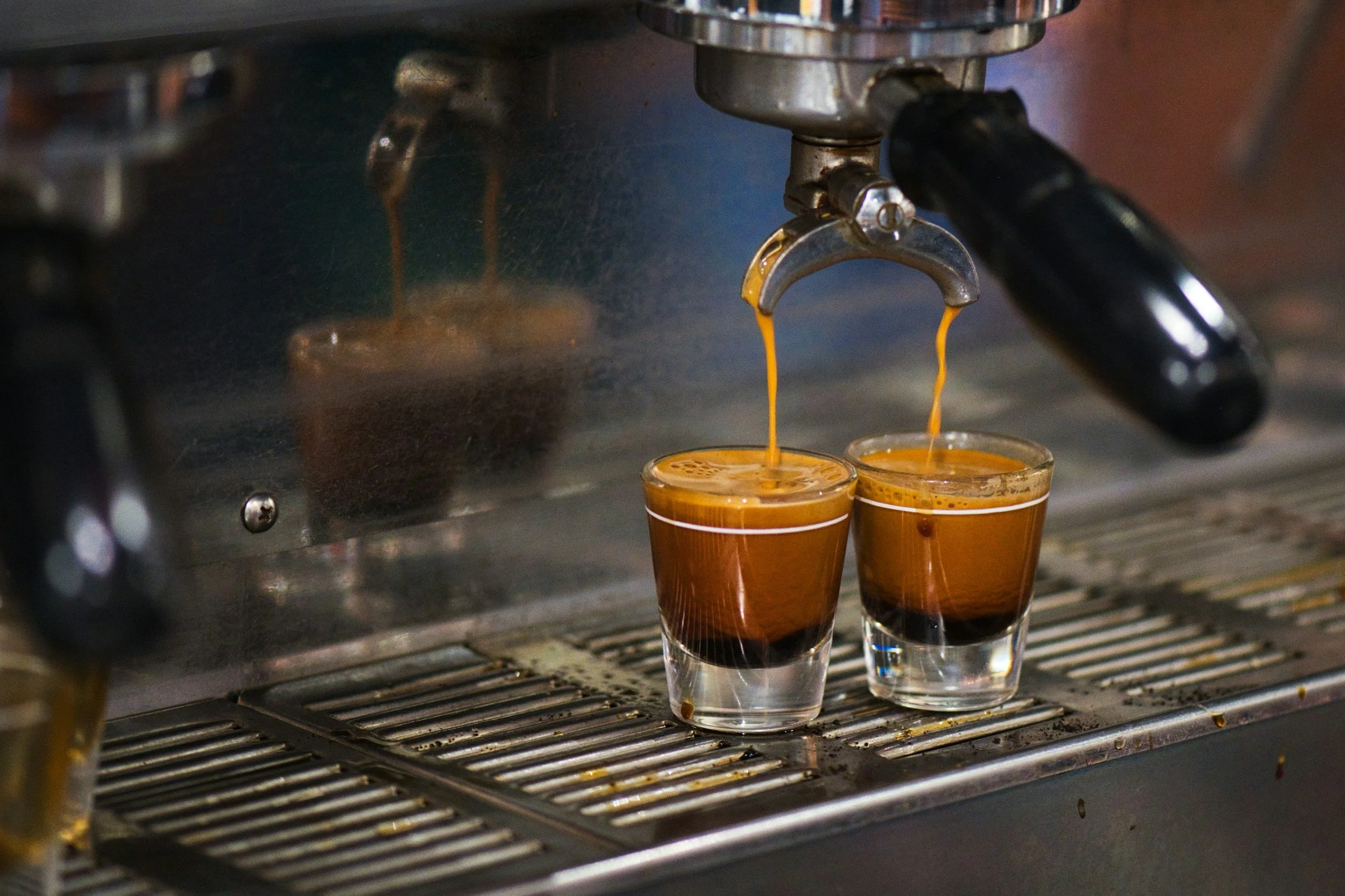Espresso shots being pulled from a coffee machine into two small glass cups.