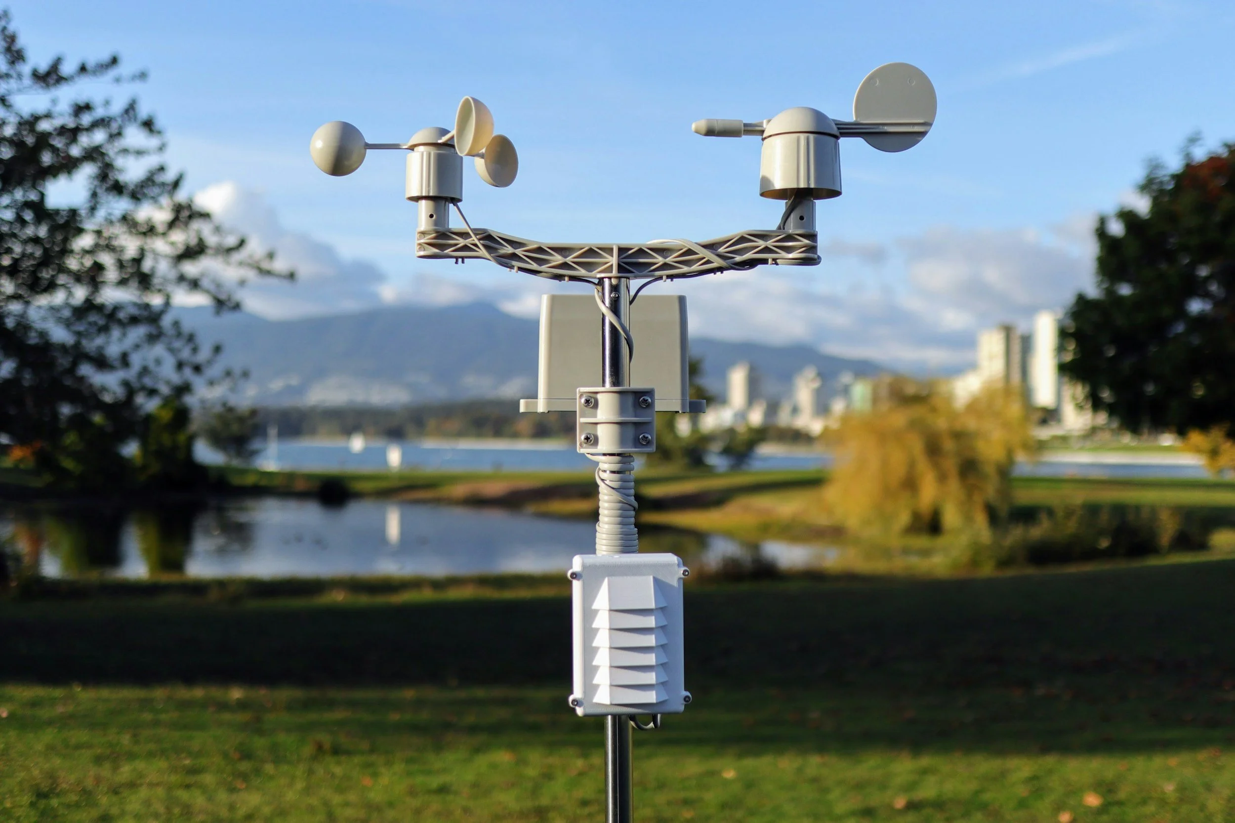 Meteorological instruments on a stand with a river, city skyline, and mountains in the background.