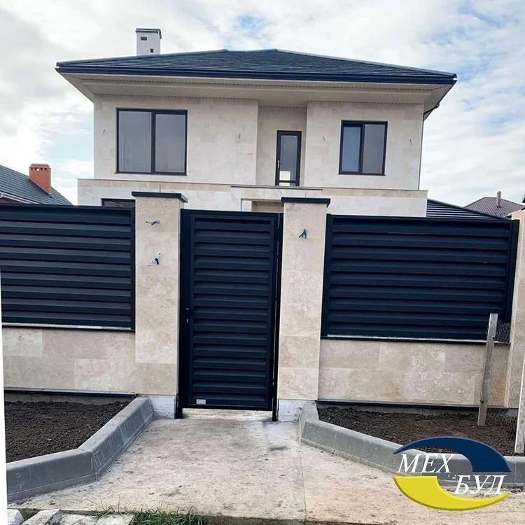 Maison moderne avec clôture noire et porte en métal, devant un trottoir en béton.