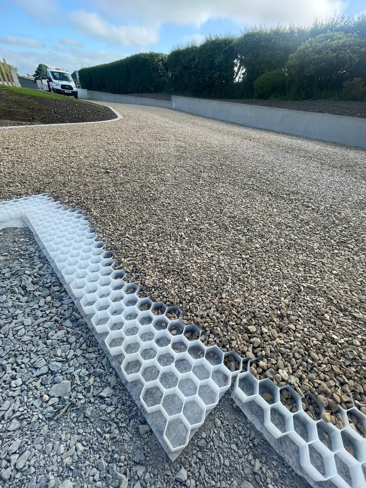 Travaux de construction d'un chemin avec un revêtement en gravier et un système de drainage en plastique blanc avec une grille hexagonale.