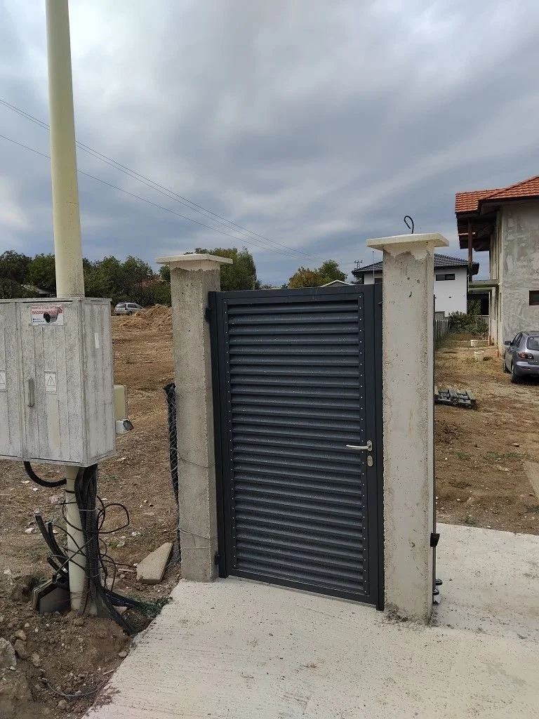 Portail noir en métal dans une clôture en béton, situé devant un terrain en construction ou en préparation
