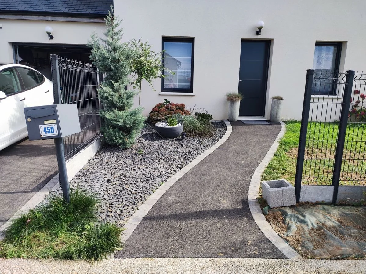 Allée pavée menant à une porte d'entrée de maison, avec des plantes et un arbre décoratif