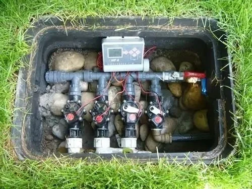 Un système d'irrigation enterré avec plusieurs vannes, tubes, capteurs, et un contrôleur électronique dans une tranchée recouverte d'herbe.