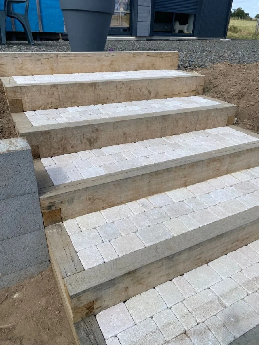 Escaliers en cours de construction avec poutres en bois et pavés blanc cassé.