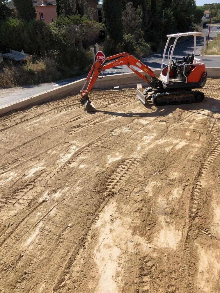 Mini-pelle orange sur un terrain de construction avec des marques de pneus dans la terre, zone en cours de préparation pour un aménagement.