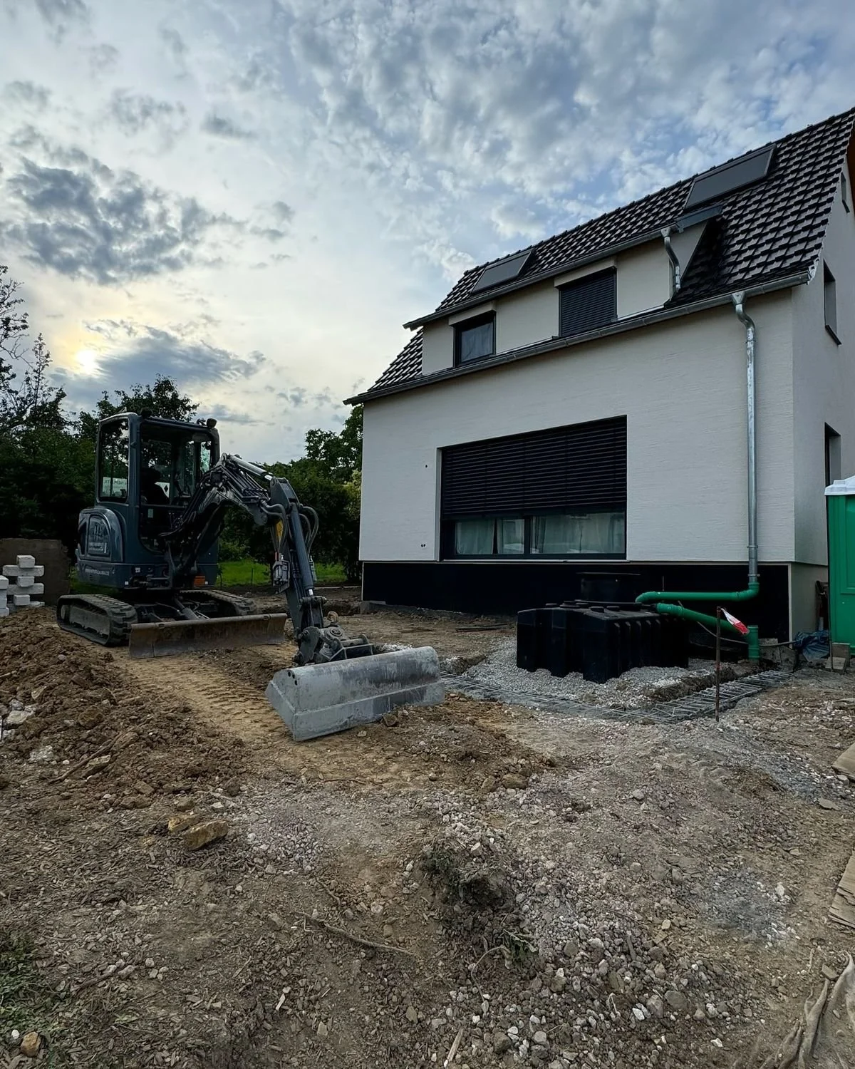 Construction de terrasse ou de fondations devant une maison moderne blanche avec un petit excavateur sur le chantier.