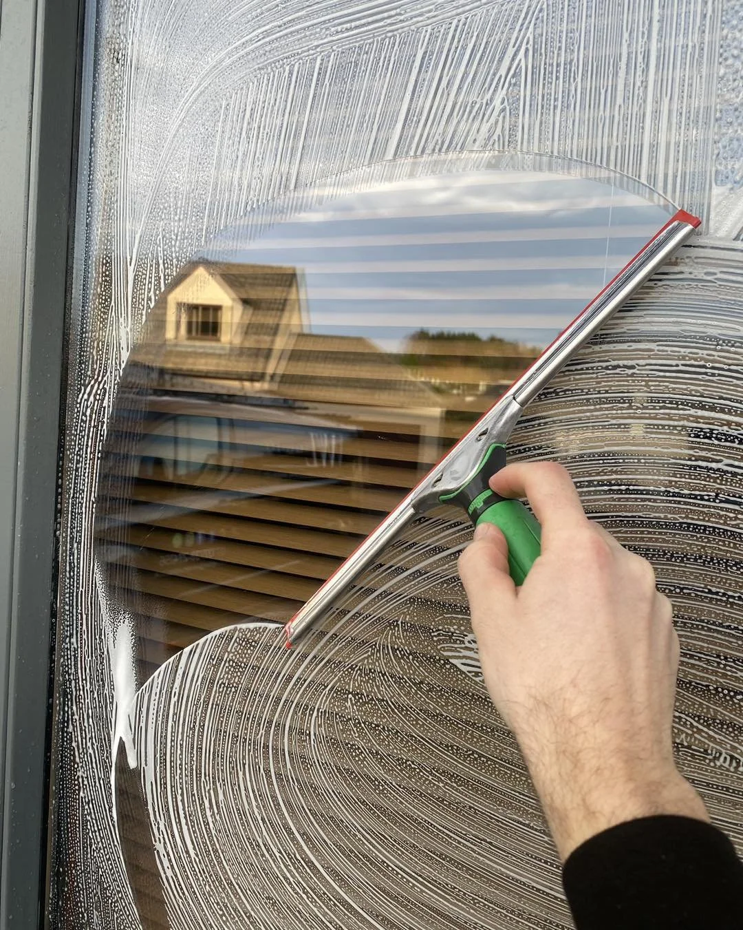 A person cleaning a window with a squeegee, leaving a streak-free area on the glass.