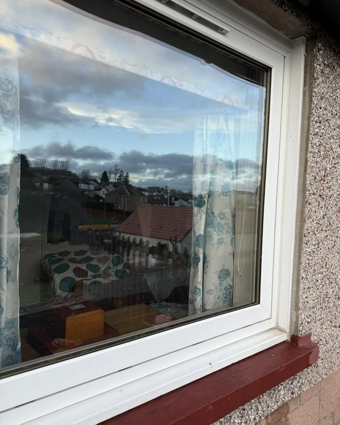 View through a window showing a cloudy sky and a neighborhood with houses and trees.