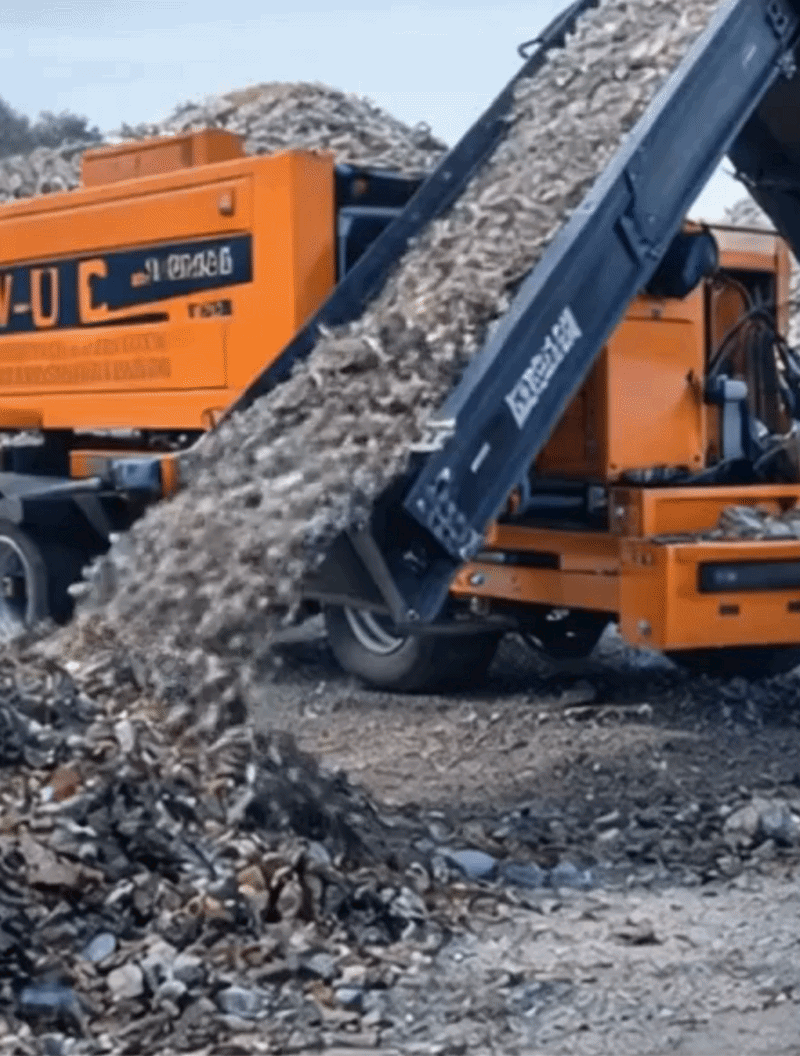 Une machine de chantier en train de décharger des débris ou des déchets de construction, avec des piles de matériaux en arrière-plan. Broyeuse Doppstadt.