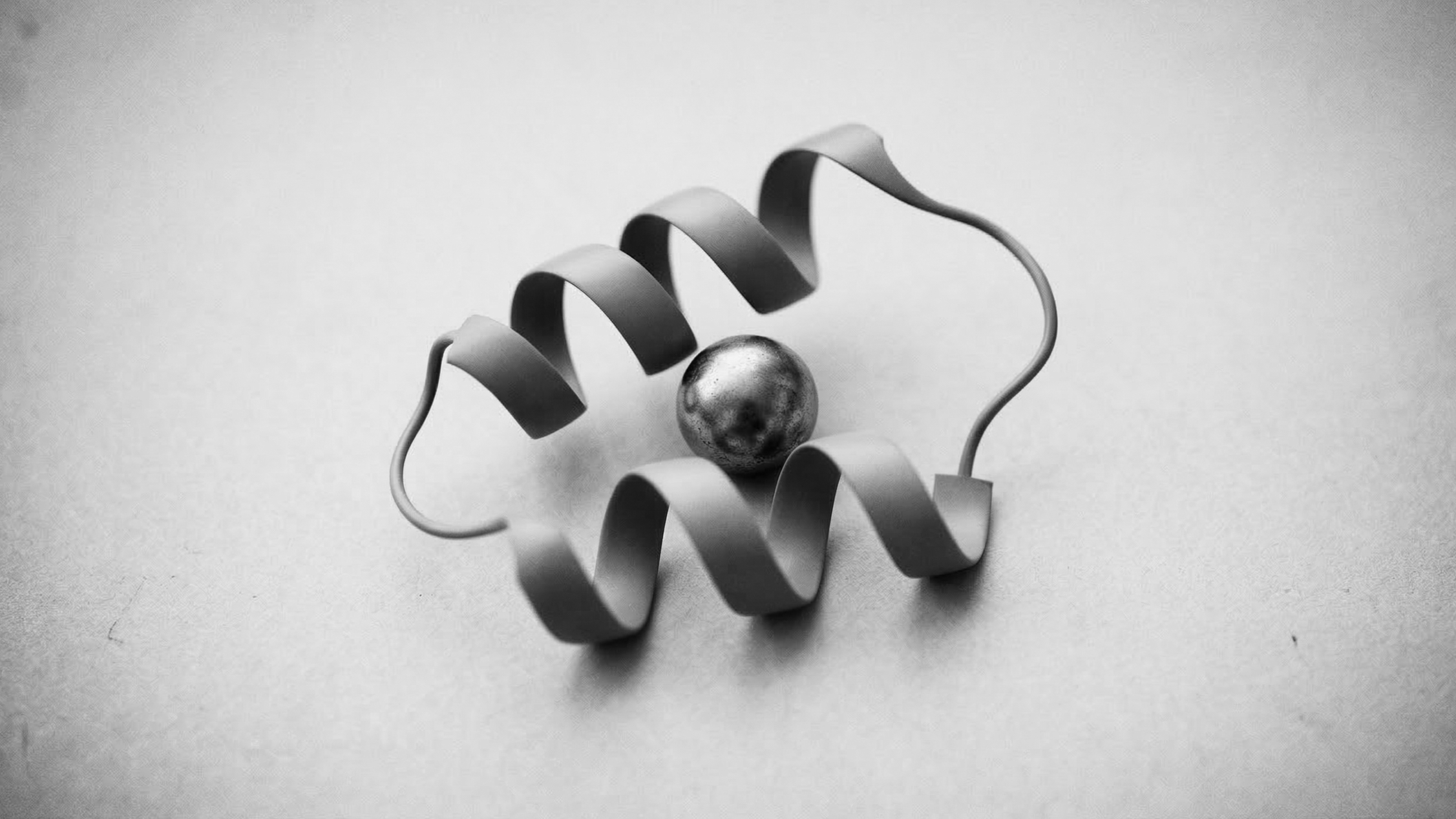 A metallic marble with a reflective surface surrounded by a spiral metal wire on a plain background.