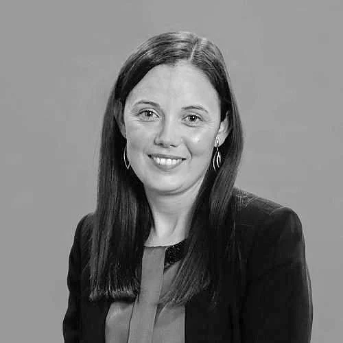 Black and white photo of a woman with long dark hair, wearing a blazer and earrings, smiling at the camera.