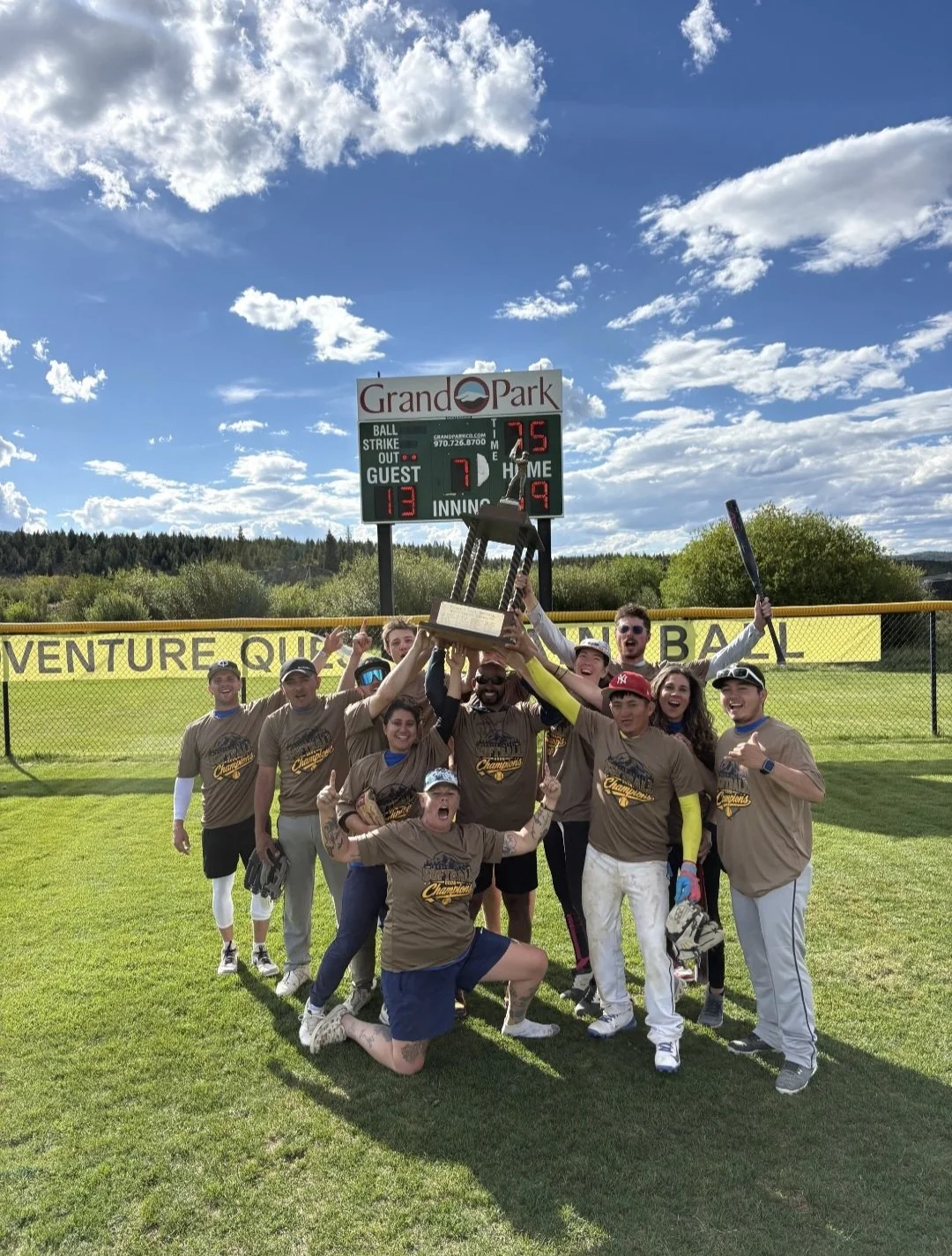 Sals Team, celebrating with the trophy after winning the comp league, scoreboard in the background showing a win, clear sky and trees. Vamos!
