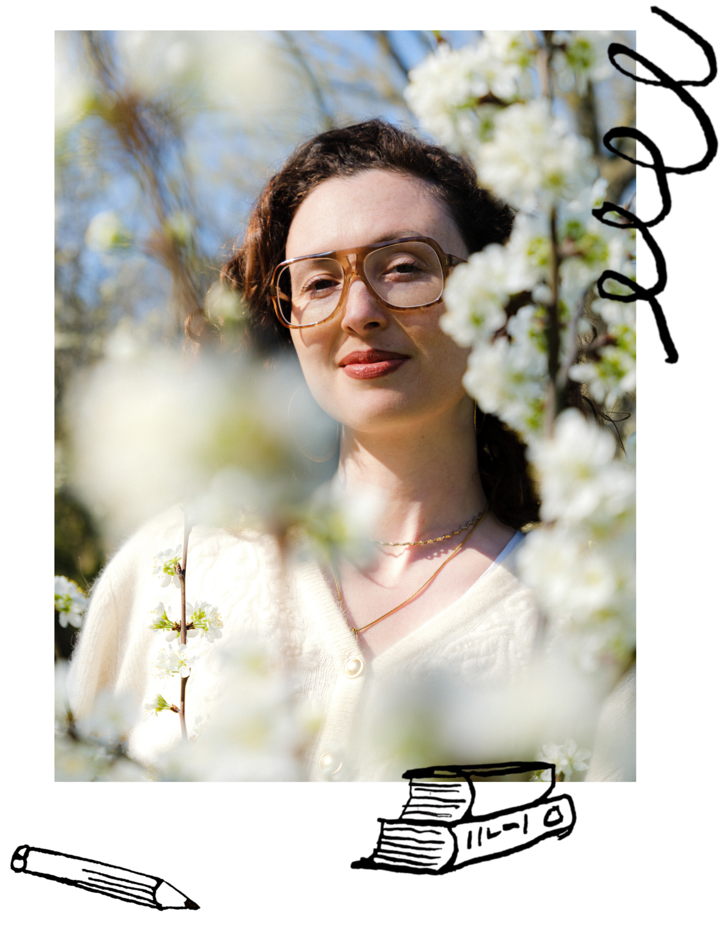 A woman with curly brown hair and glasses standing among blooming white flowers outdoors on a sunny day.