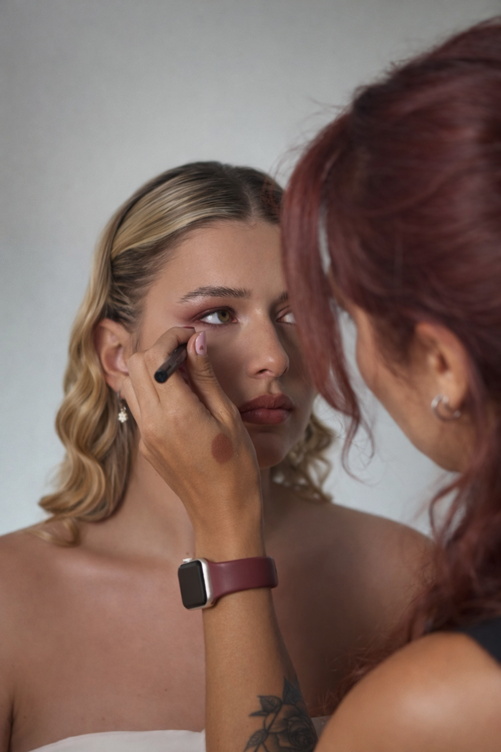Makeup artist applying eye makeup to a young woman with blonde hair.