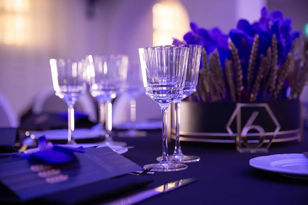 Eleganter Gästetisch mit dekorativen Gläsern, Blau- und Lilaton, Blumen und Platzkarten bei einer Feier
