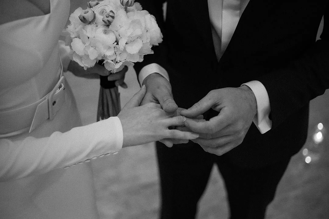 Ein Heiratsantrag bei einer Hochzeit, bei dem ein Mann einer Frau einen Heiratsring an den Finger steckt, während das Paar eine Blume hält.