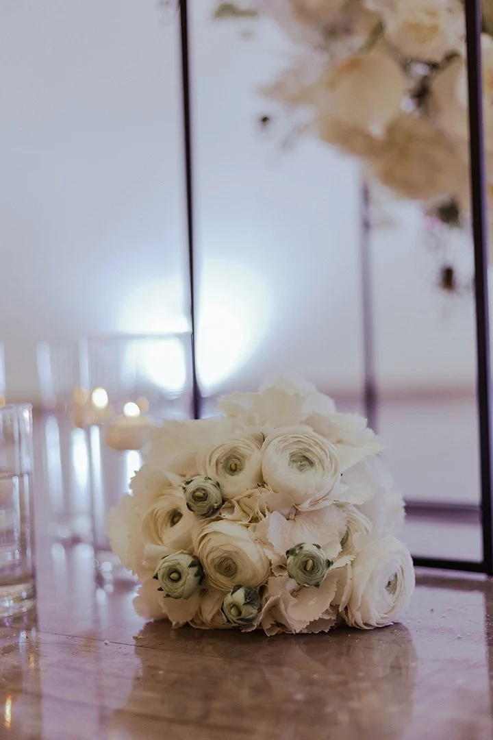 Blumenbouquet mit weißen und grauen Blüten auf einem Holztisch, im Hintergrund Spiegelflächen und Gläser