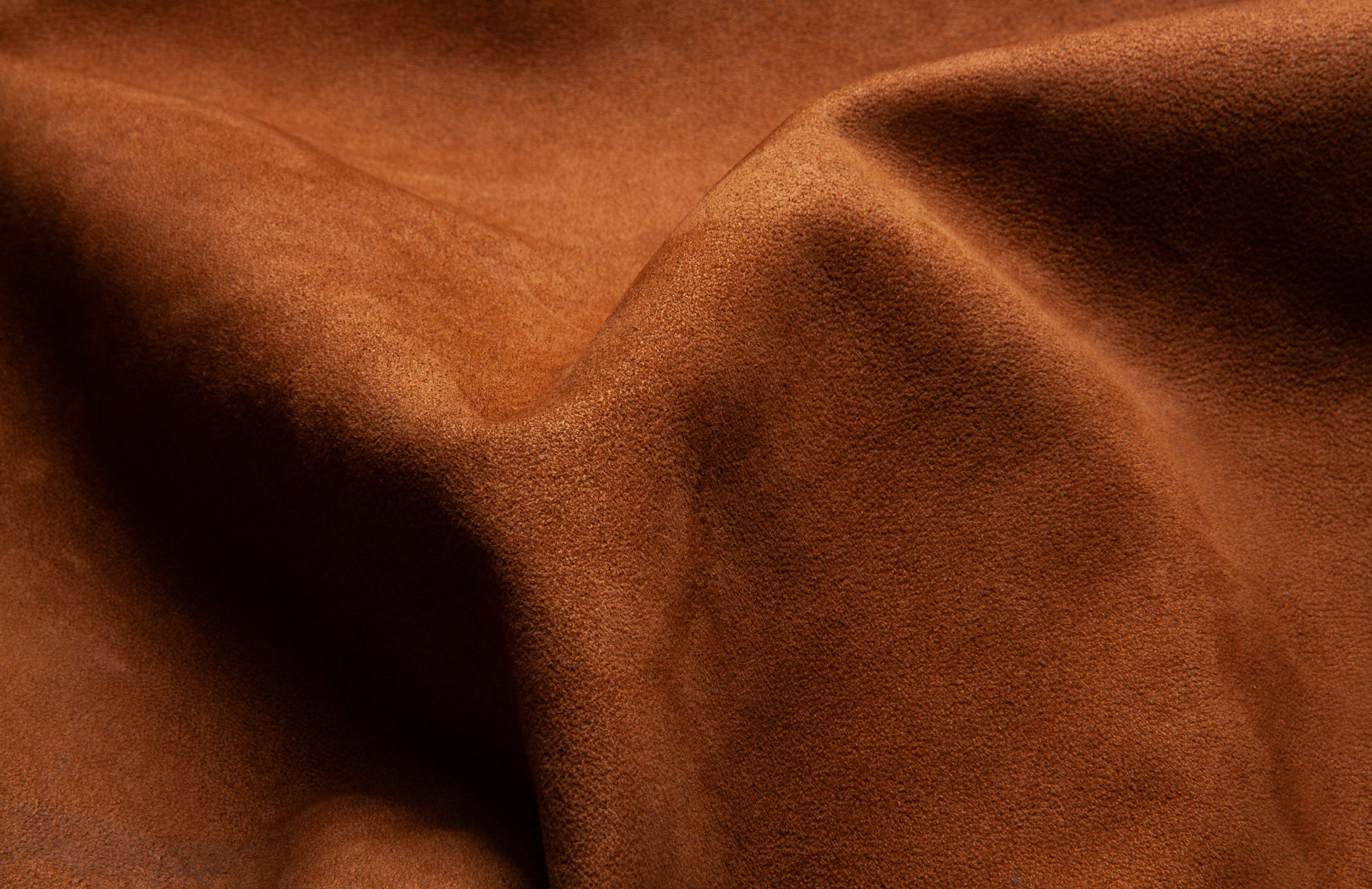 Close-up of brown suede fabric with soft texture and gentle folds.