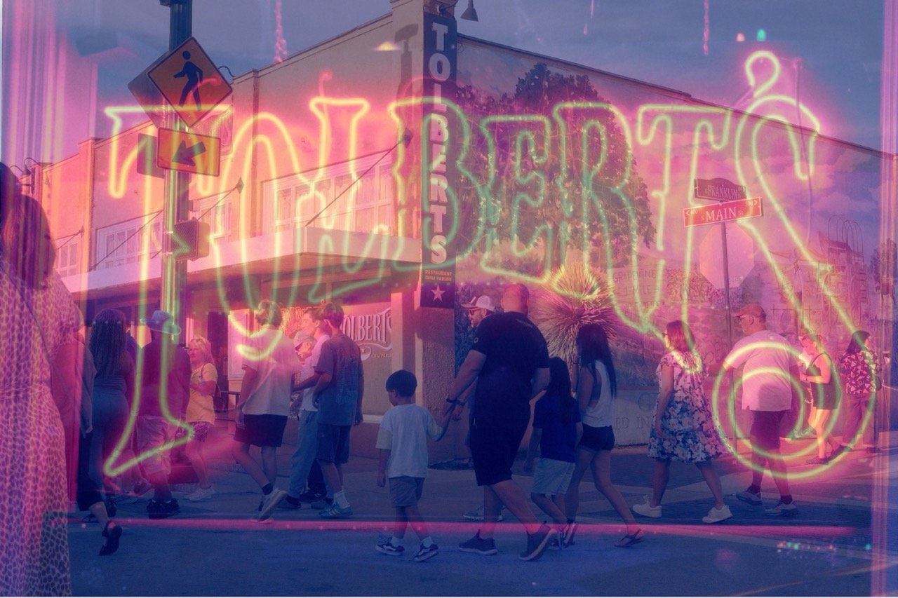 A neon sign reading 'FREAKS' overlays a street scene with people walking past a store, fireworks in the sky, and street signs for 'FREAKING' and 'MAIN' street.