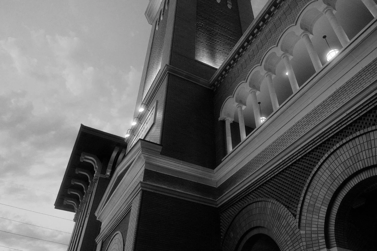 A black and white photograph of a building with classical architectural features, including columns and arches, taken from a low angle during the daytime.