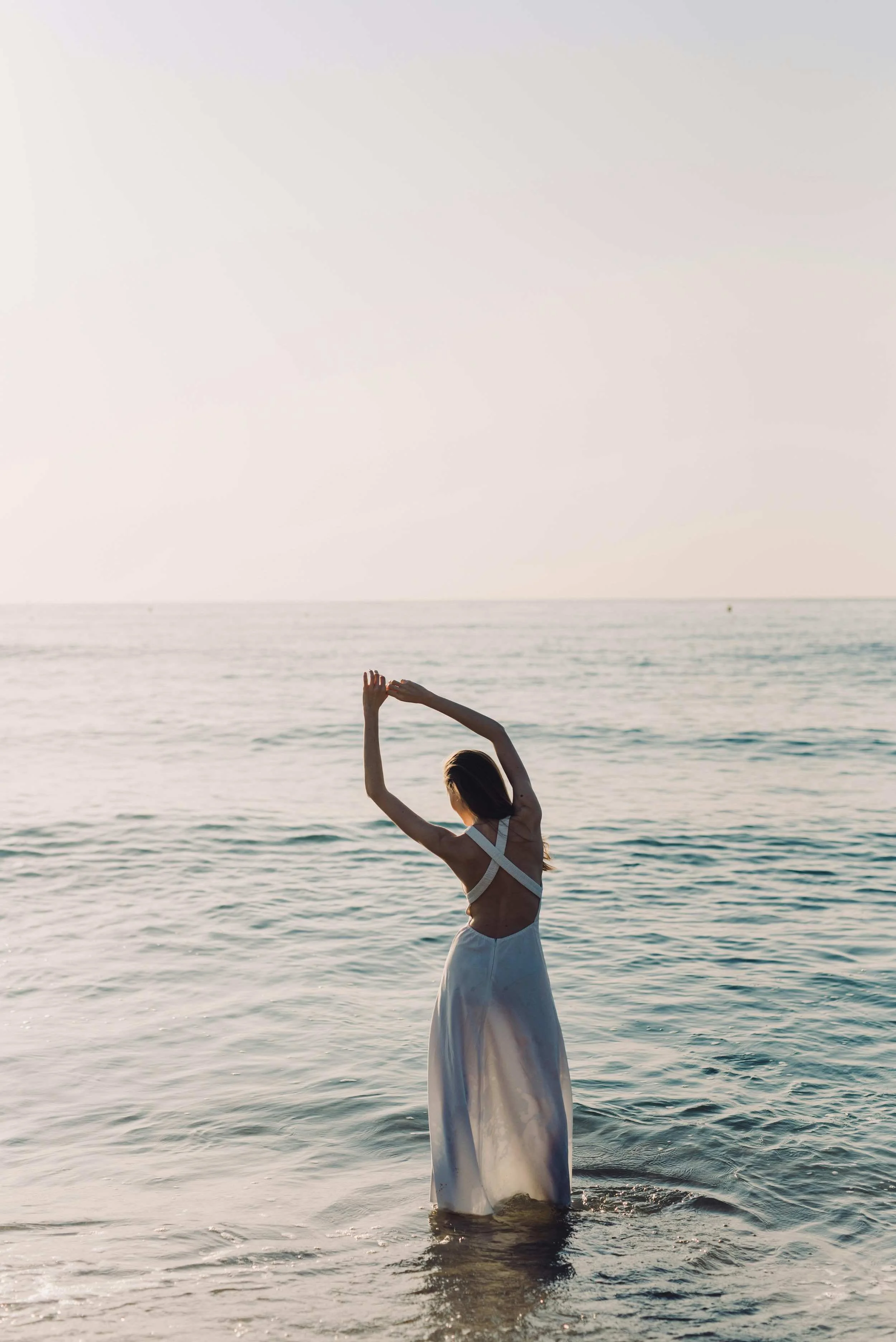 Young woman on a beach, stretching while diving her feet in the sea.