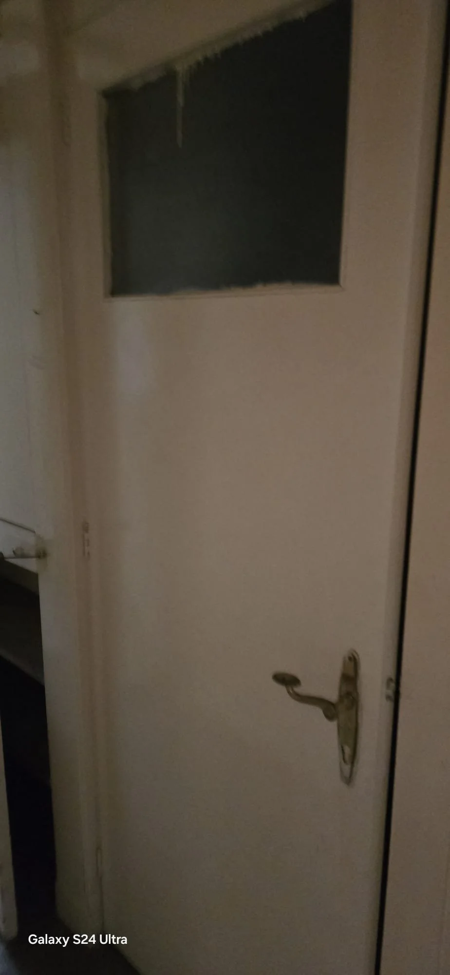 Een witte deur met een raam bovenaan en een deurknop aan de rechterkant.