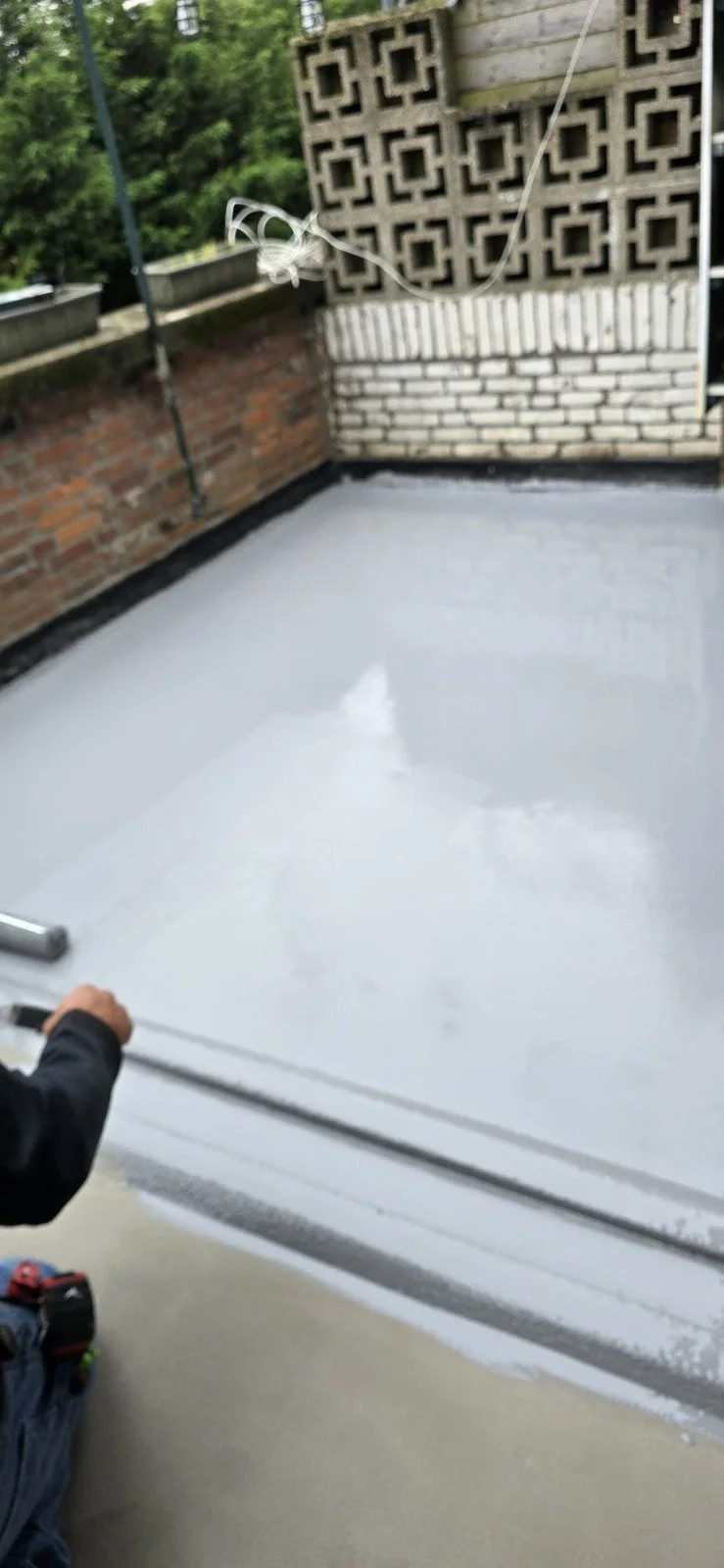 Tegelwerk en een geïsoleerde witte dakbedekking op een balkon of dakterras, met een person die een rol raamfolie aanbrengt.