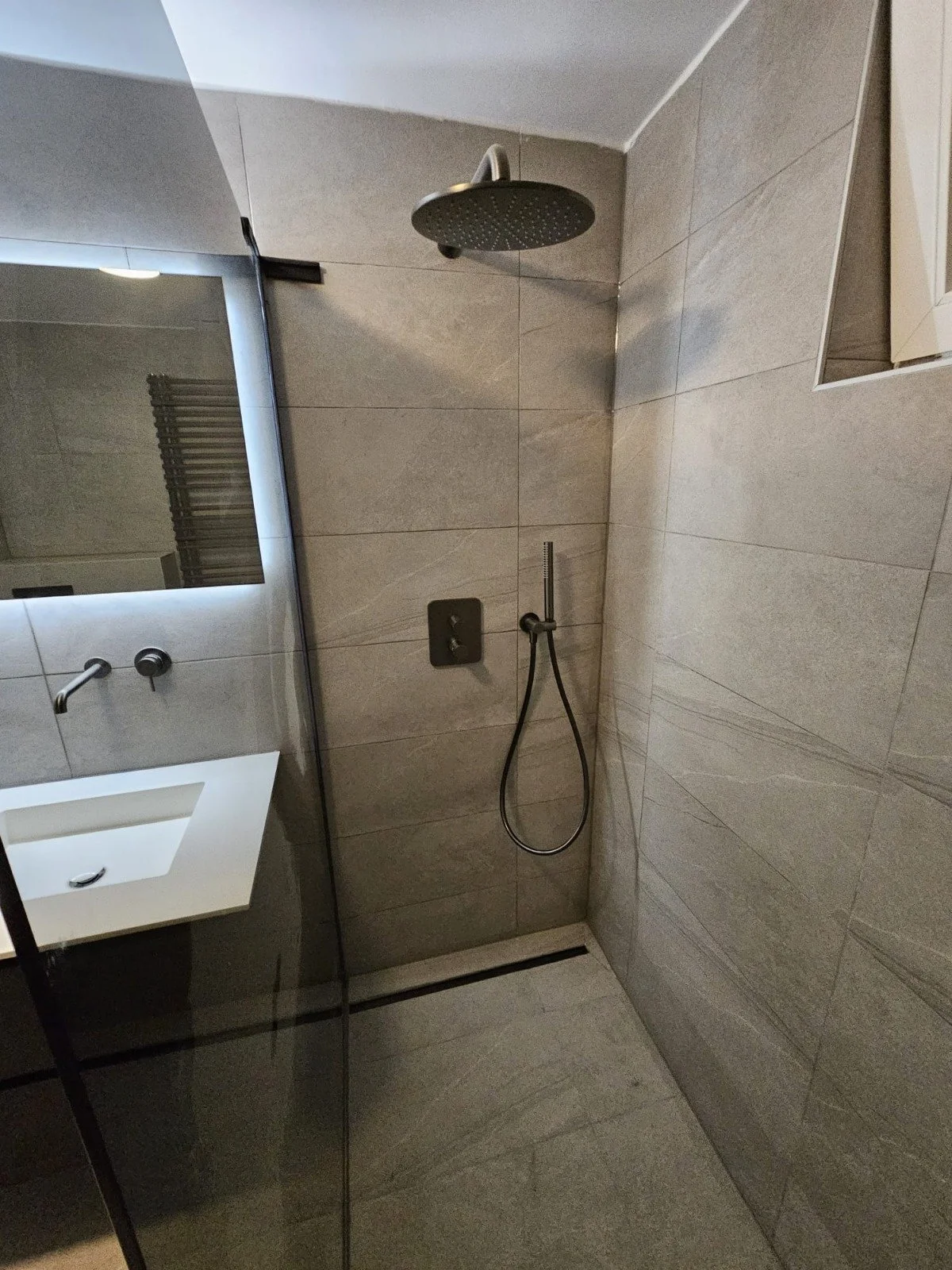 Moderne badkamer met inloopdouche, regen douchekop en handdouche, betegeld in grijstinten.