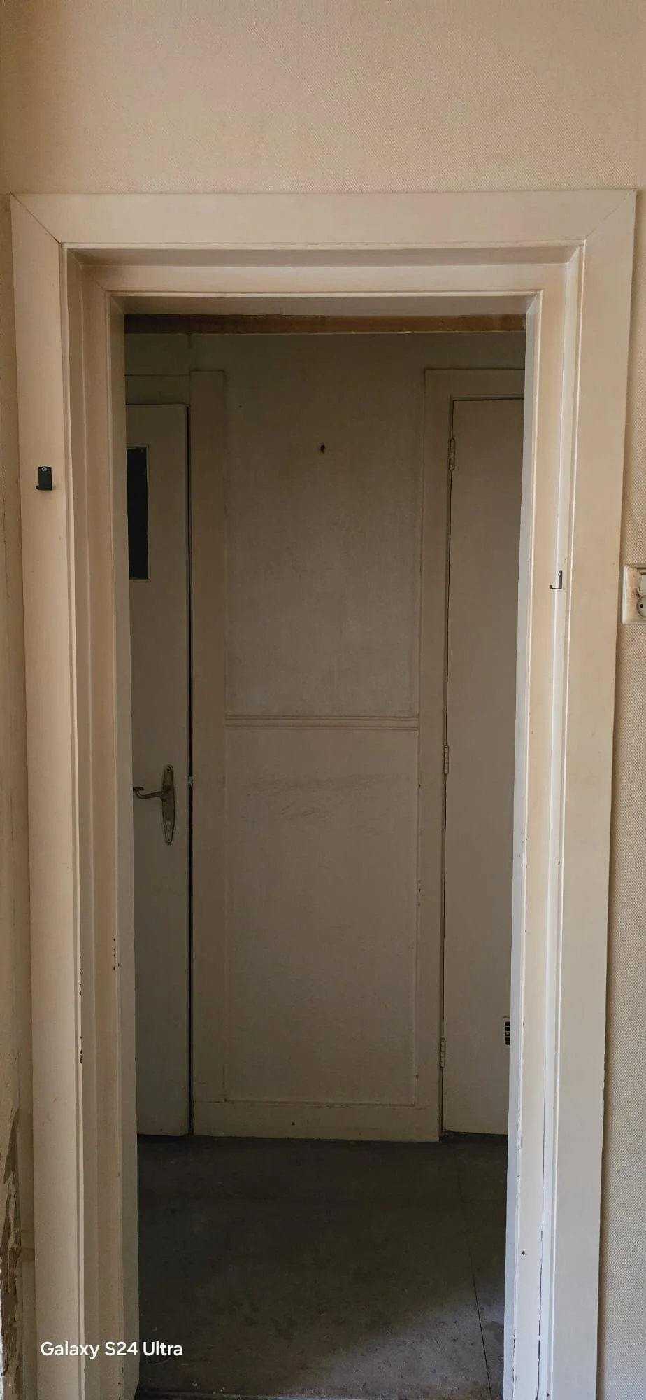 Een deur die open staat, leidt naar een donkere kamer met een witte dubbele deur.