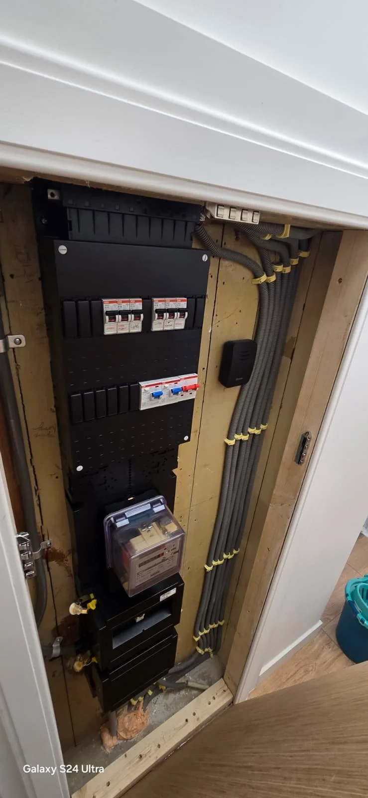 Elektriciteitskast met schakelaars, kabels en een meter, geïnstalleerd in een houten kast.