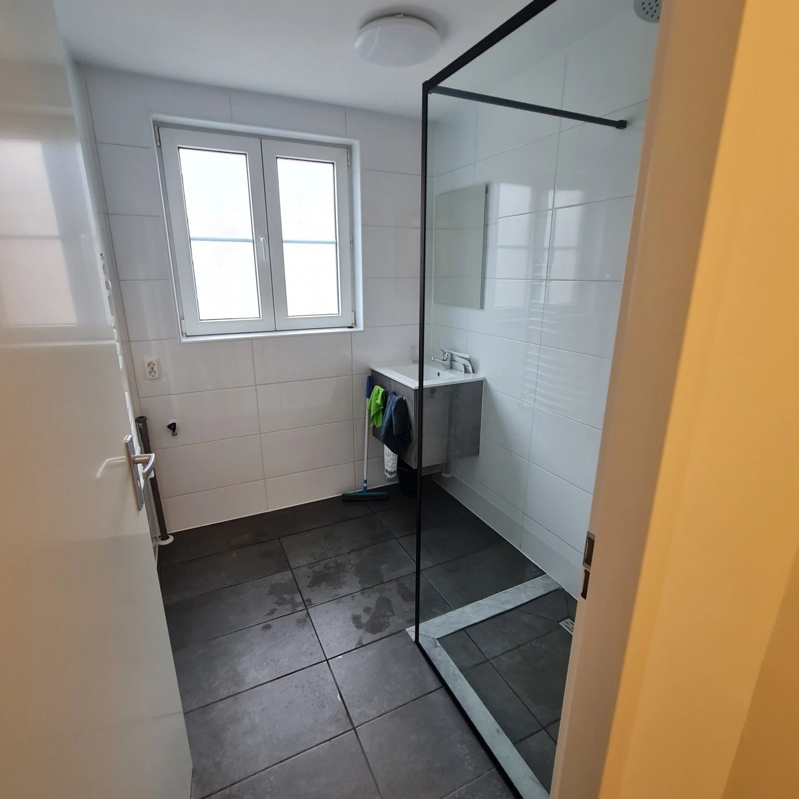 Een badkamer met een douchecabine, een wastafel met spiegel, een raam, en vloer- en muurtegels in zwart en wit.