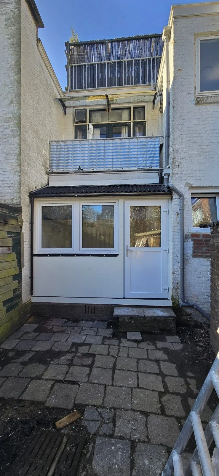 De achtergevel van een rijtjeshuis met een veranda, een balkon en een dakterras.