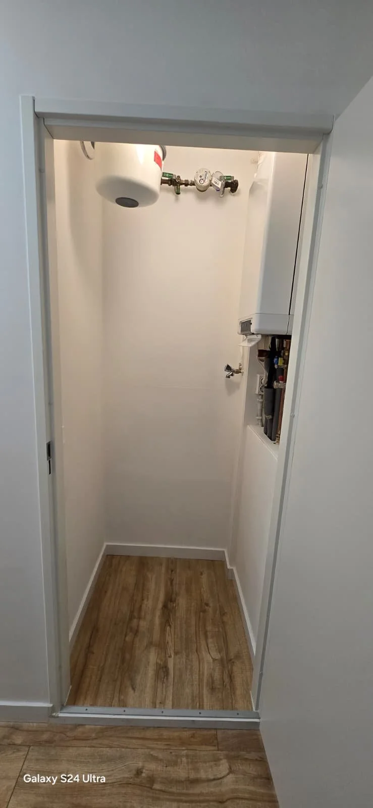 Een kleine, leegkast met waterleidingen en een boiler of verwarmingswaterkoker.