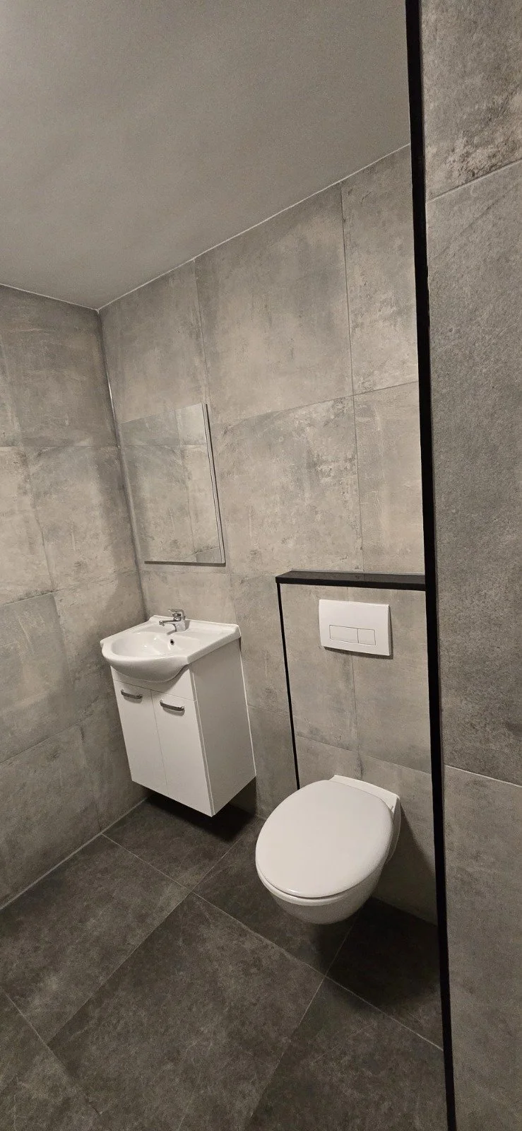 Een modern toilet en wastafel in een badkamer met grijze tegels en een spiegel.