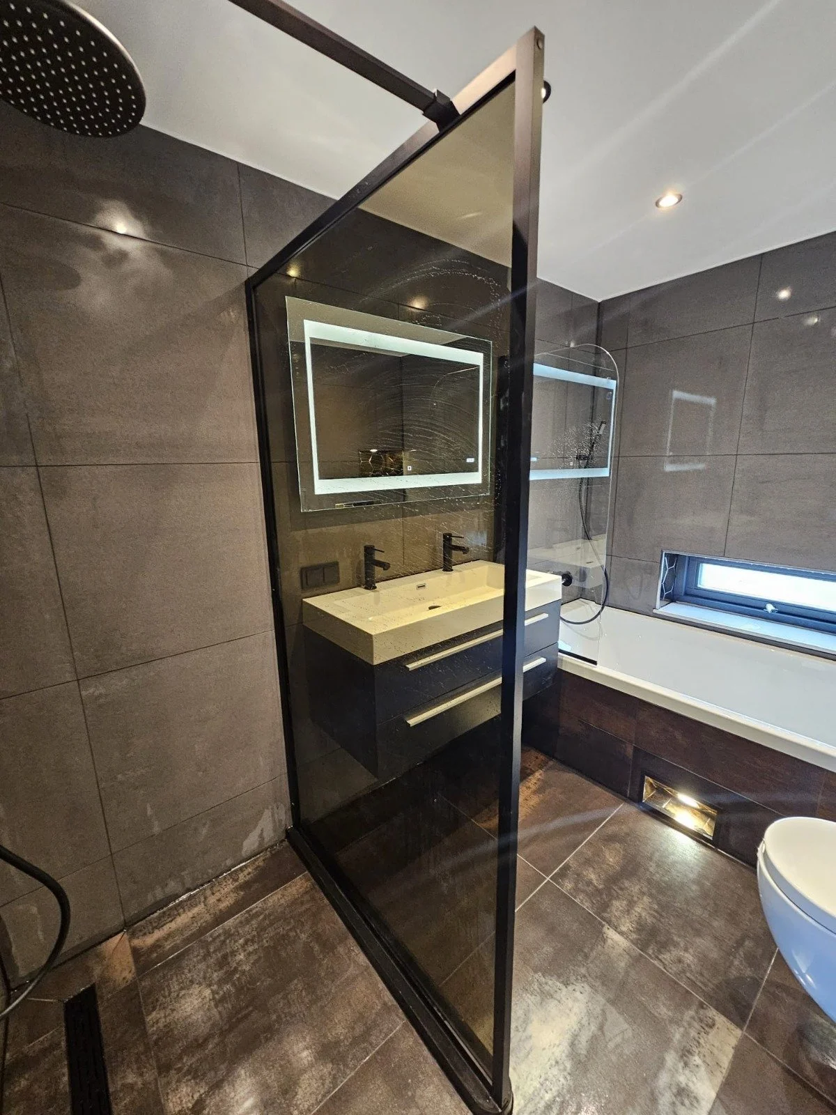 Moderne badkamer met een inloopdouche, dubbele wastafel met spiegel, bad en kleine raam.